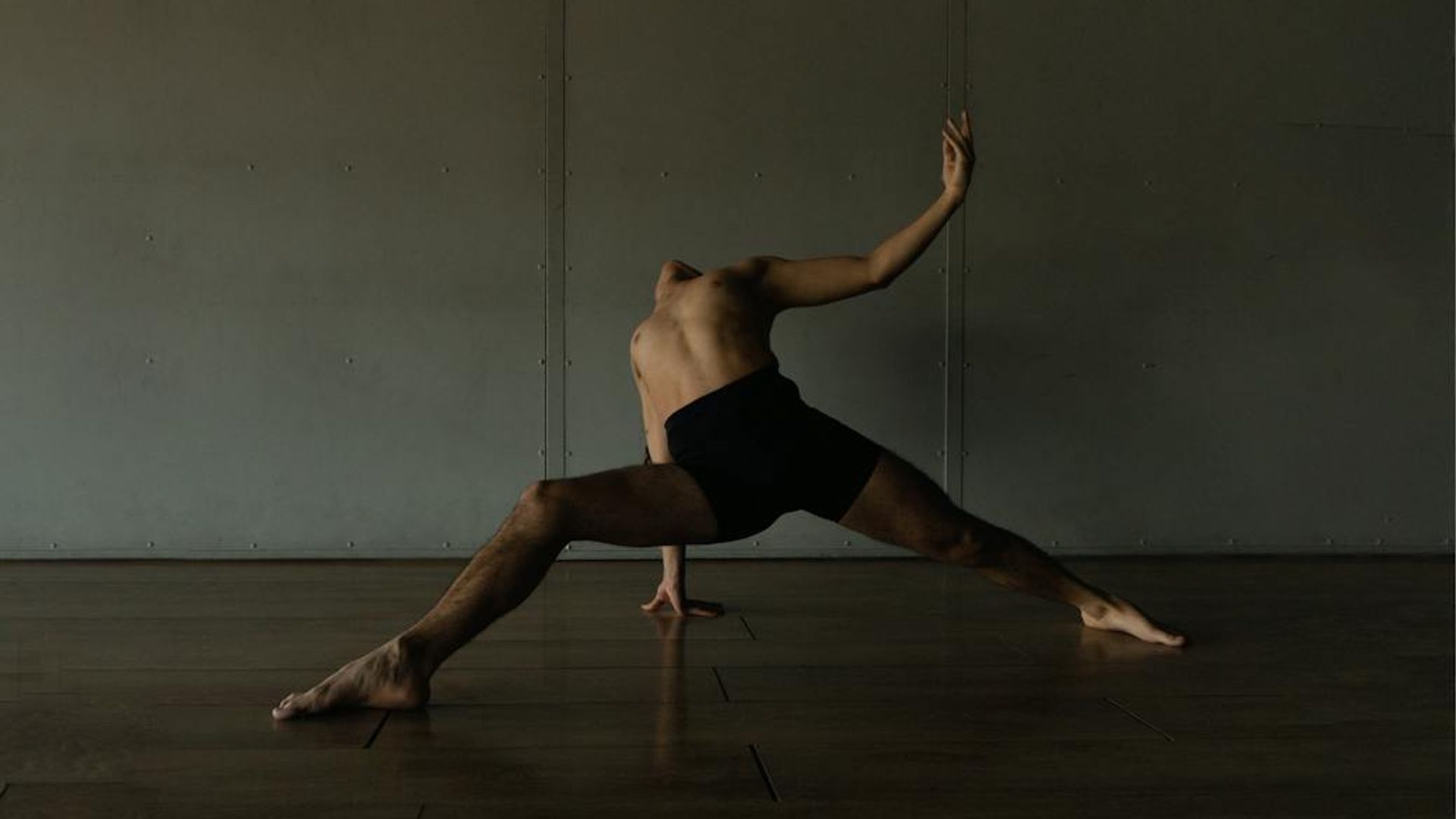 Person performing a serene yoga movement in a minimalist dark studio.